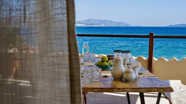 A table with a view of the sea, a wooden railing, and a table setting including a bowl of fruit, glasses, and white teapots. - Sunrise Hotel (Samos)