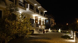 A multi-story building with a stone-paved courtyard, balconies, and a well-lit entrance. - Sunrise Hotel (Samos)