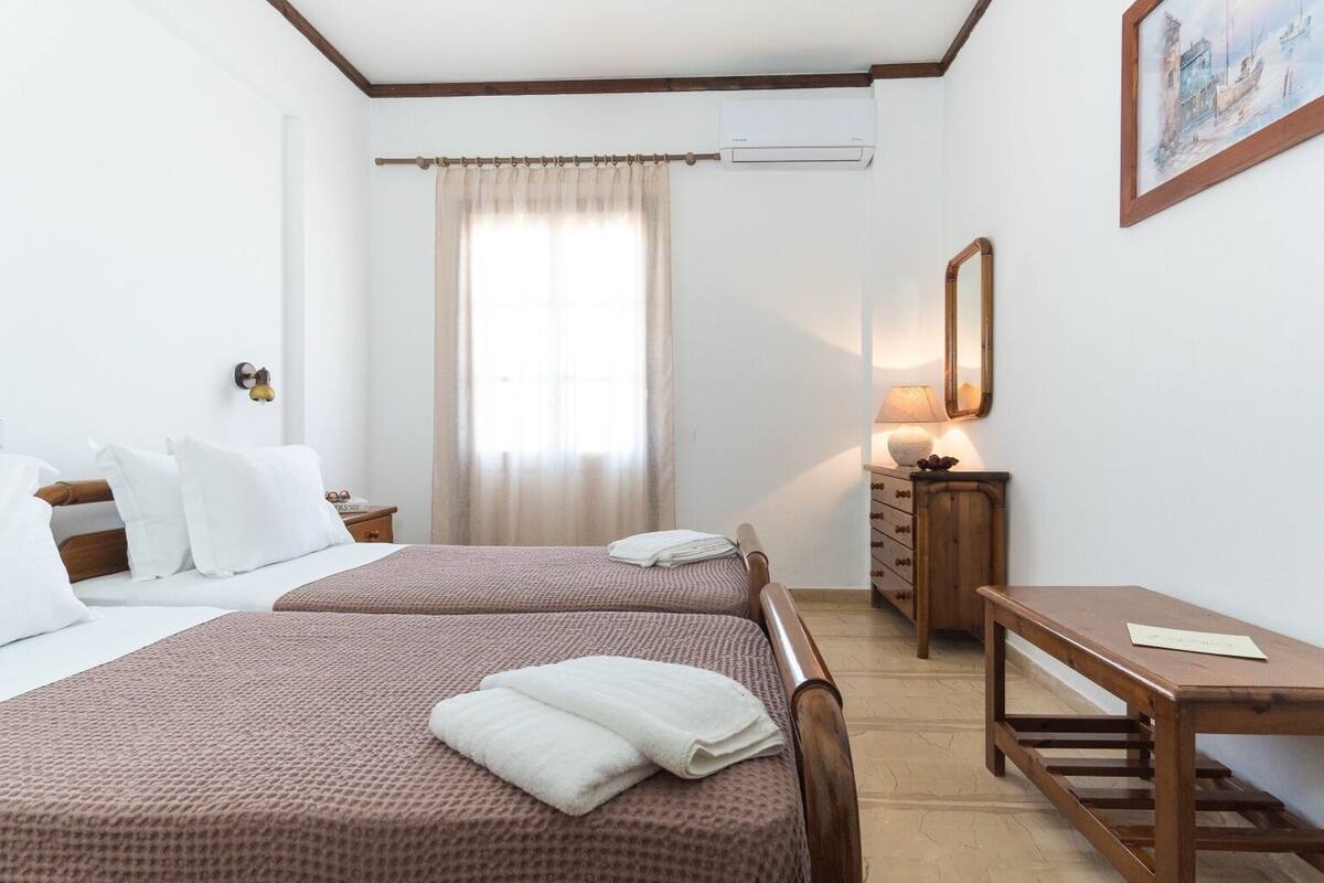 Hotellihuone, jossa on kaksi sänkyä, työpöytä, peili ja ikkuna, jossa on verhot.