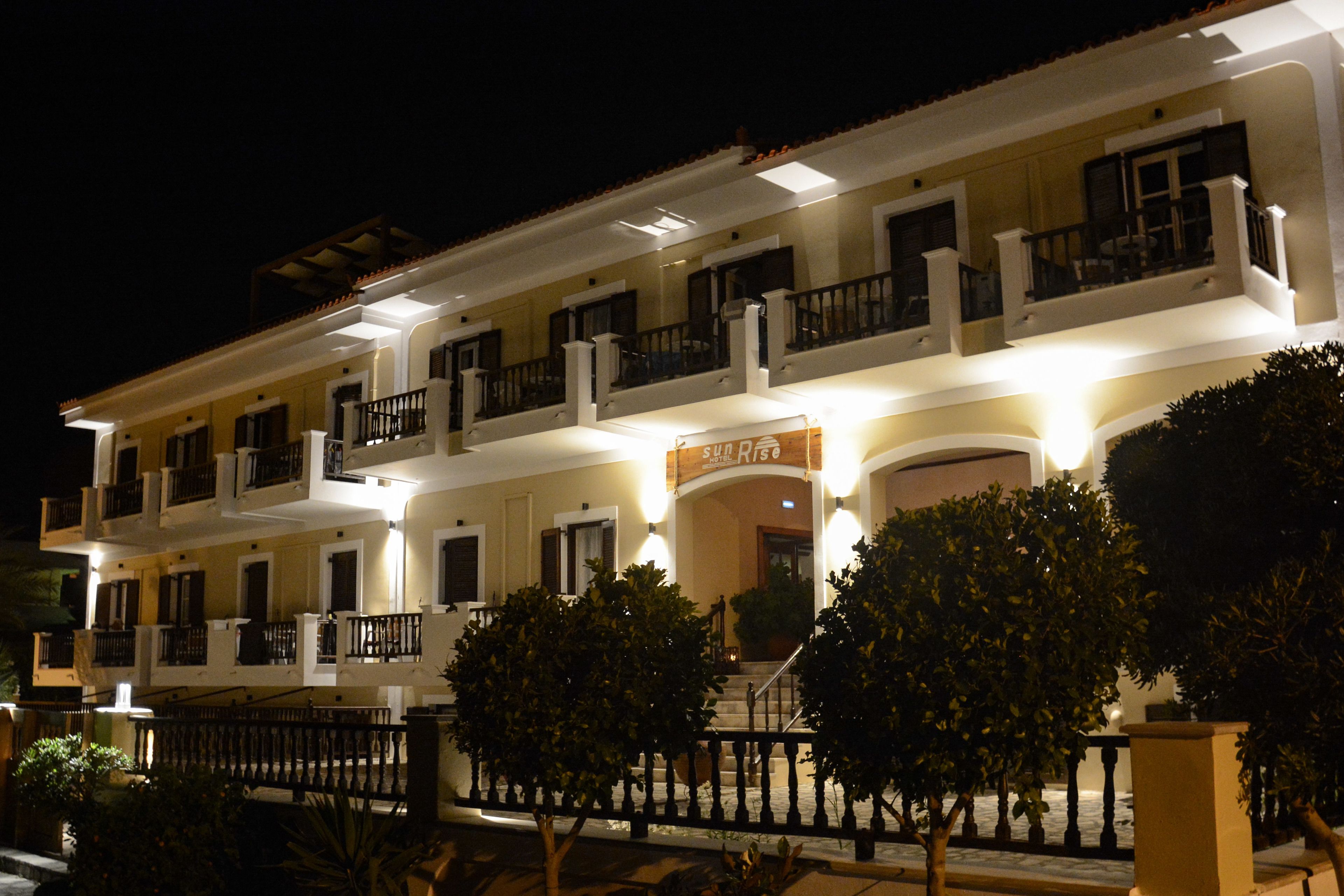 Un hotel de varios pisos con balcones, una entrada bien iluminada y un cartel que dice "Sun Rise".