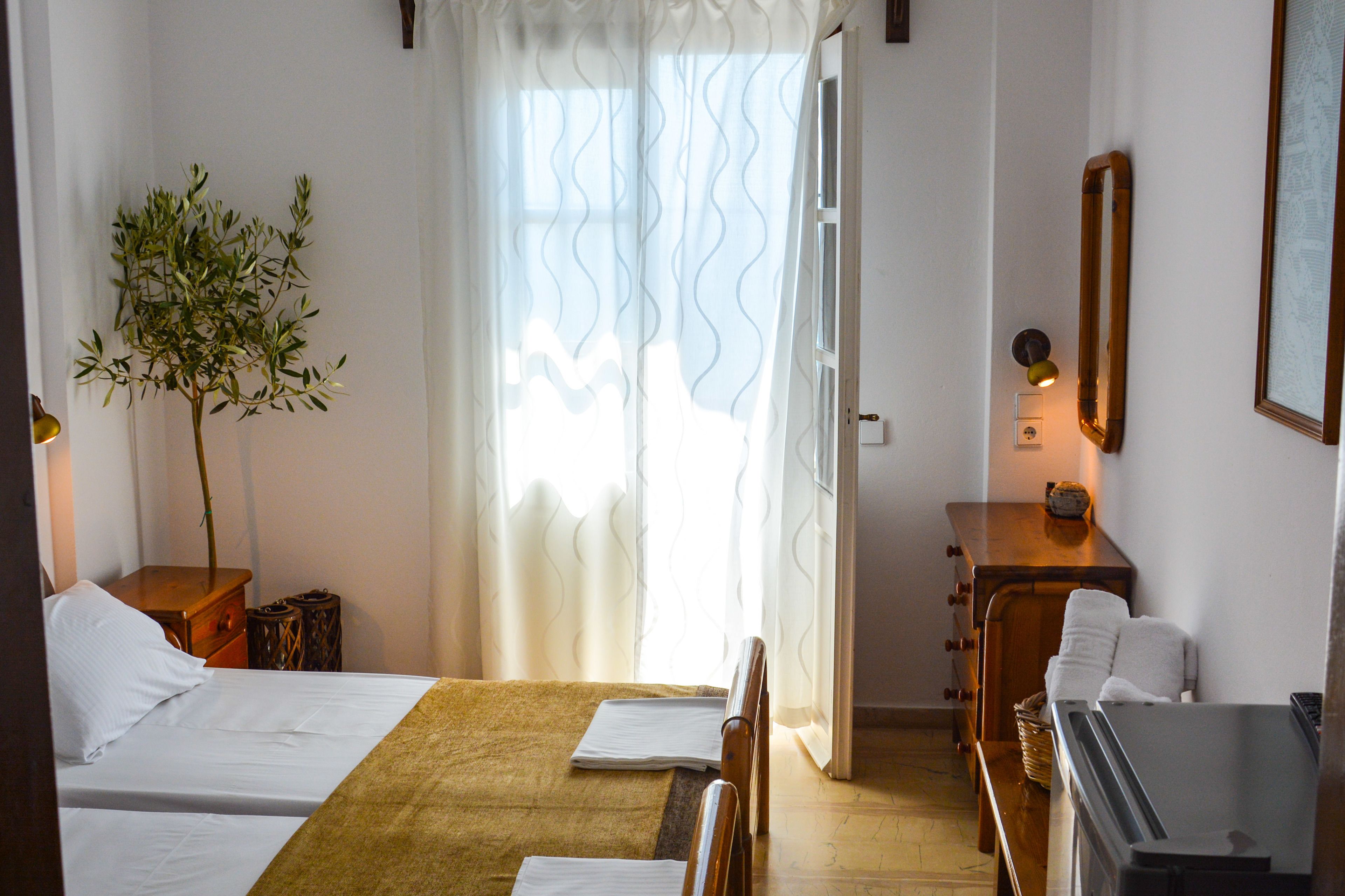 A hotel room with two beds, a wooden nightstand, a small table with a lamp, a mirror, and a window with curtains.