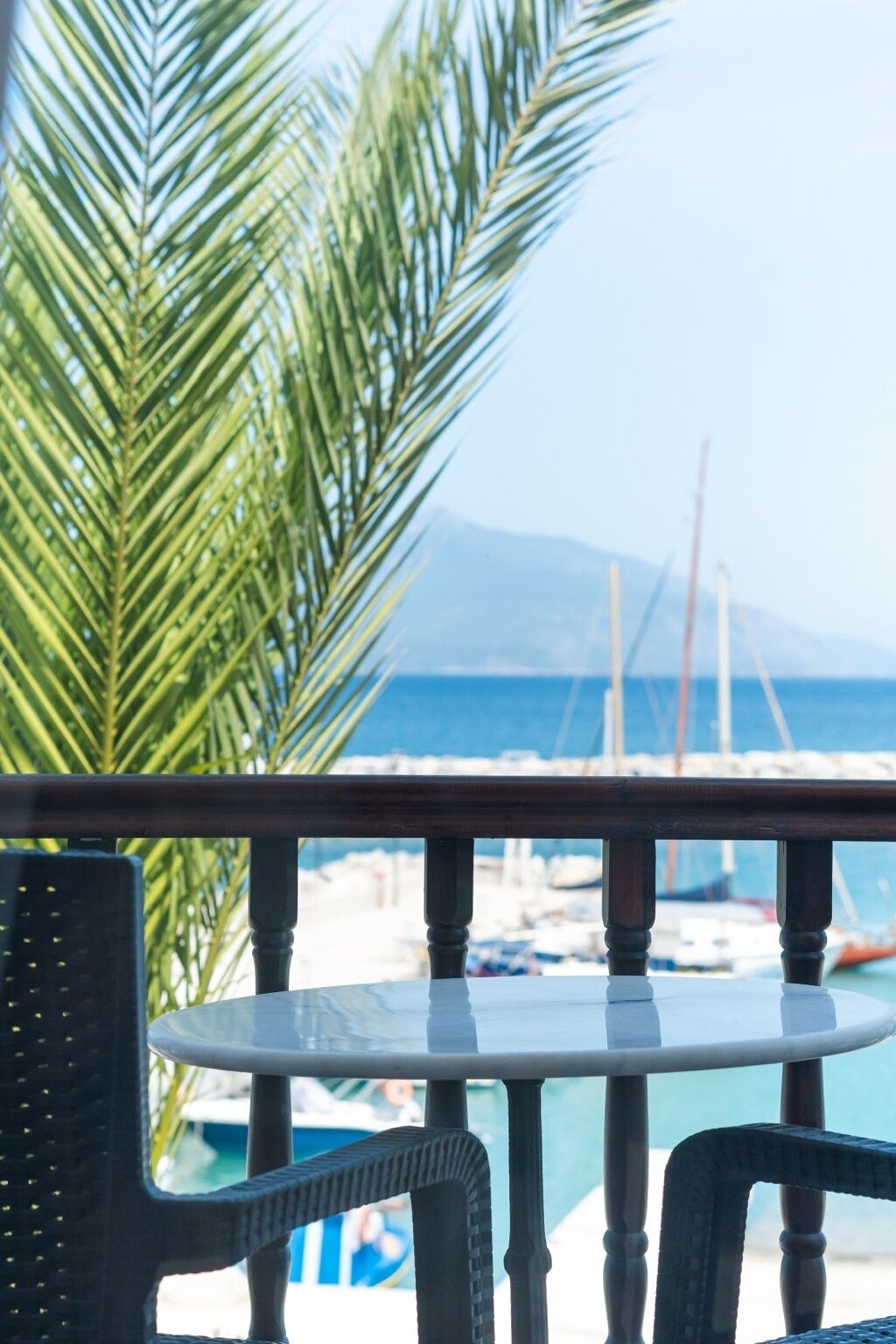 A balcony with a table and chairs, overlooking a marina with boats and a clear blue sky.