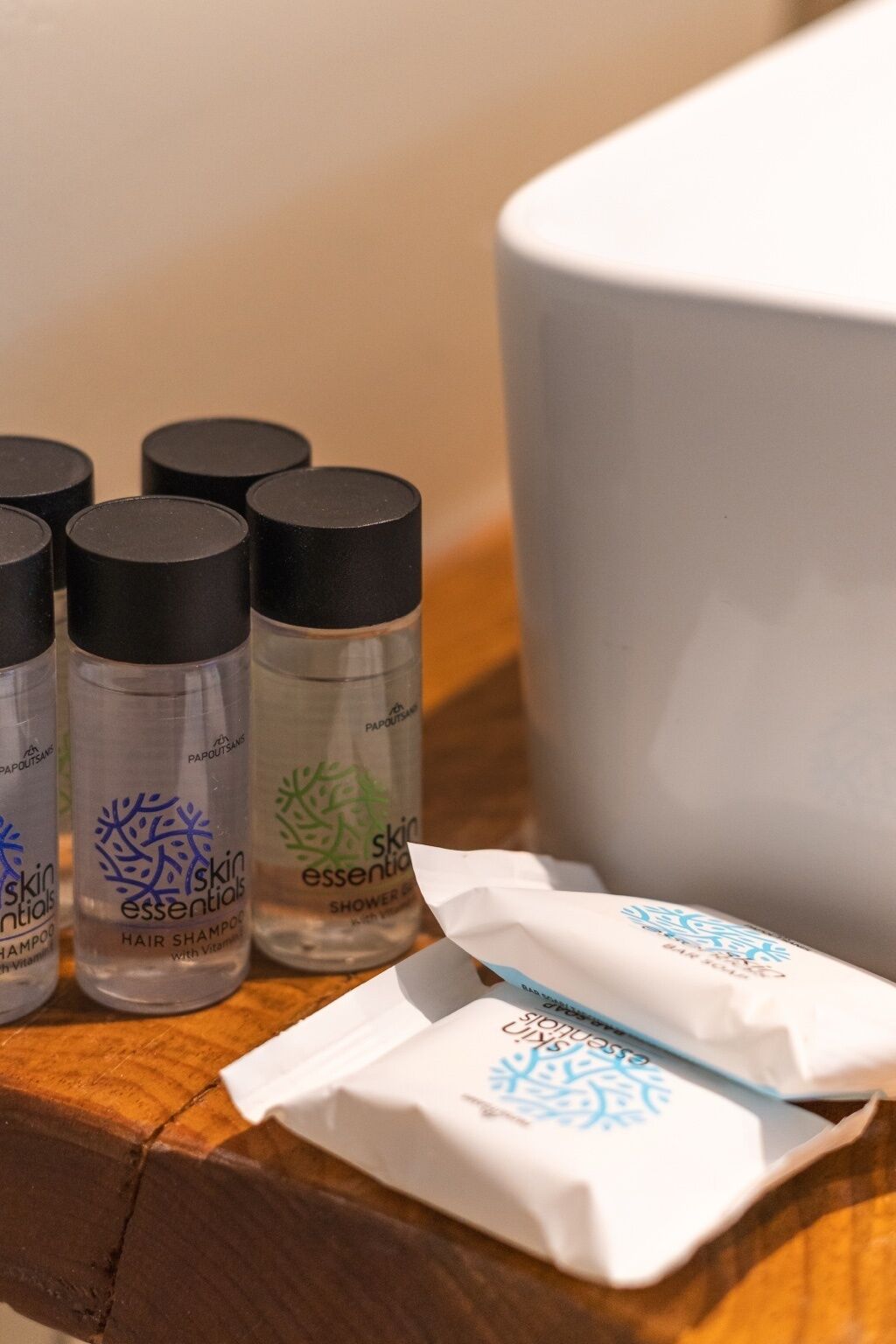 A wooden surface with bottles of skin essentials hair shampoo and shower gel, a white tissue, and a white container.