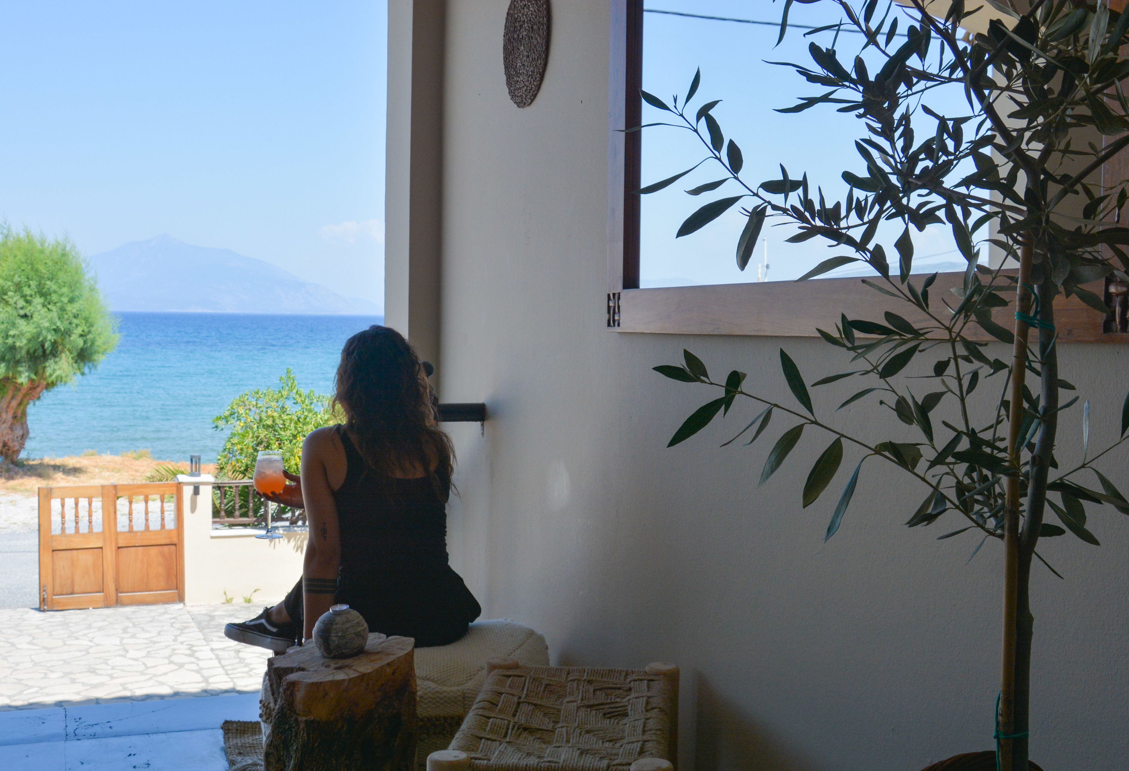 Una habitación con vista al mar, una puerta de madera, un sillón de mimbre y una planta en maceta.
