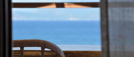 A wicker chair with a view of the ocean through a window.