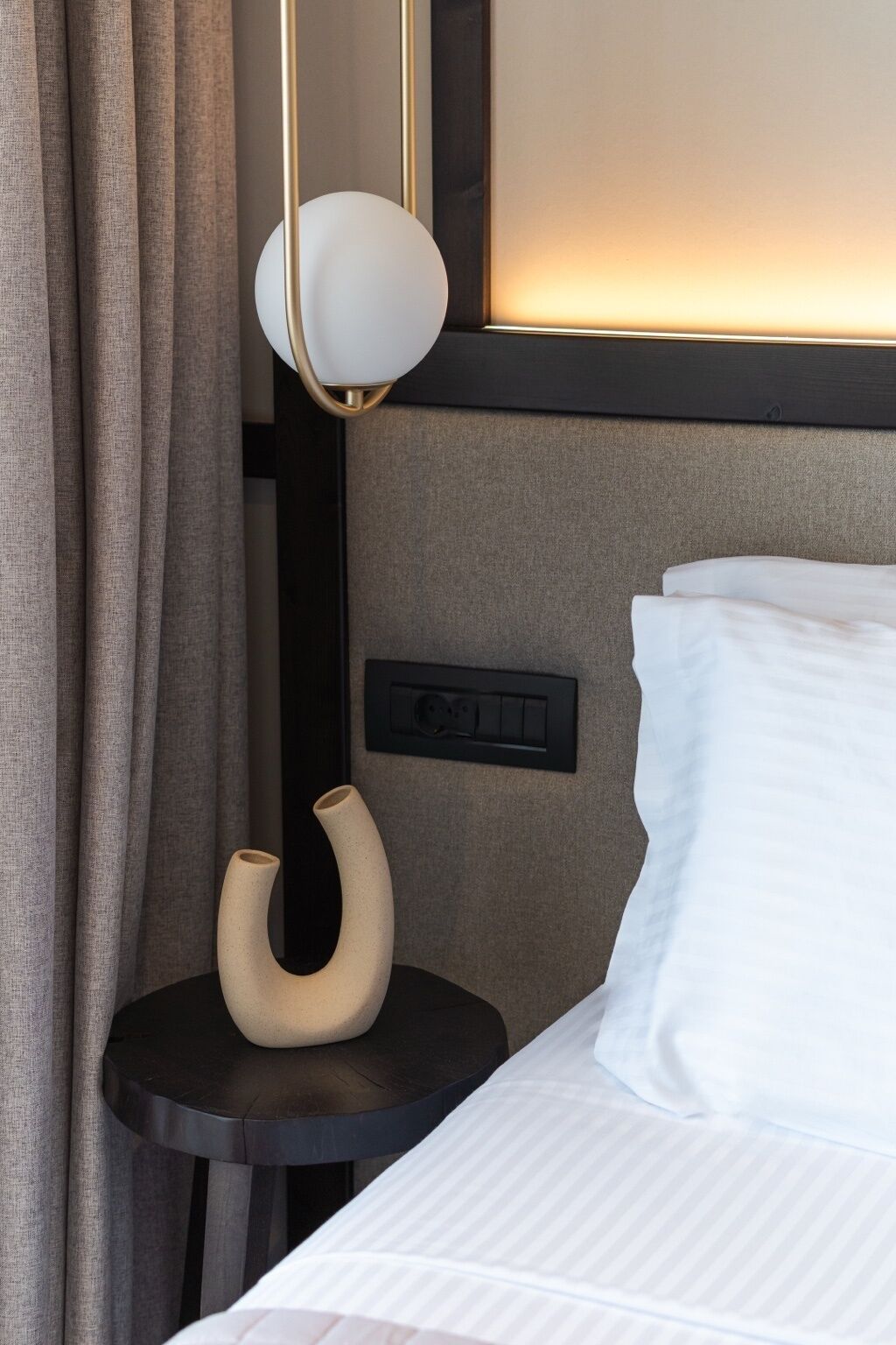 A neatly made bed with white linens, a bedside table with a vase, and a wall-mounted light fixture.