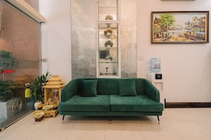 Un canapé vert dans une pièce où se trouvent une vitrine et un tableau accroché au mur.