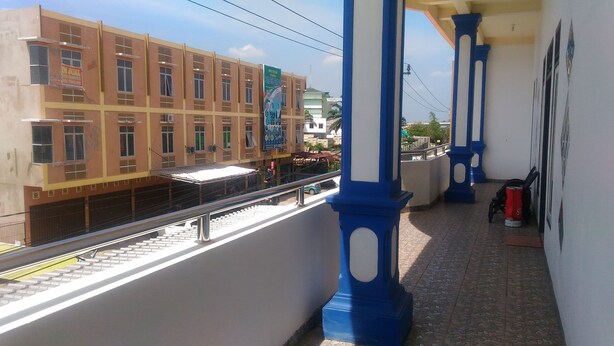 A balcony with blue columns, a tiled floor, and a view of a building with a sign. - Losmen Ibu Hj. Tarjo (Palembang)