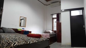 A bedroom with a bed, a bedside table, a mirror, and a window with curtains. - Losmen Ibu Hj. Tarjo (Palembang)