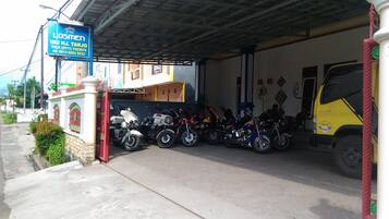 Un espace de stationnement couvert où sont garés plusieurs motocyclettes et un camion jaune, sous un abri.
