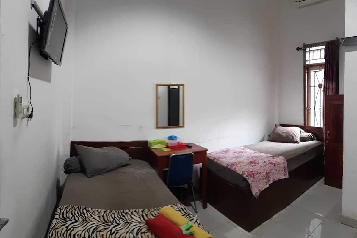 A small, clean room with two single beds, a desk, a chair, and a TV mounted on the wall.