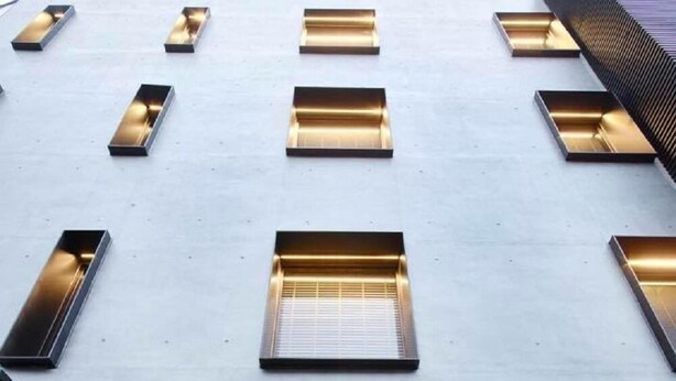 Fachada de edificio con múltiples ventanales rectangulares, algunos con estantes interiores a la vista.