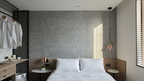 Un dormitorio moderno con una cama grande, una mesita de noche pequeña, un aparador y una ventana con persianas.