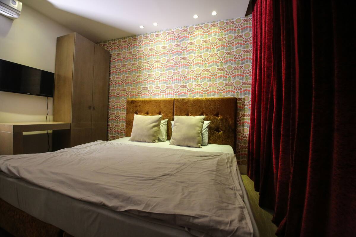Un lit bien fait, avec une tête de lit, une armoire et un téléviseur fixé au mur.