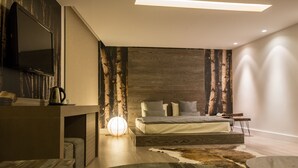 A modern bedroom with a wooden headboard, a large bed, a flat-screen TV, and a round wooden table. - Four Seasons Halat (Halat)