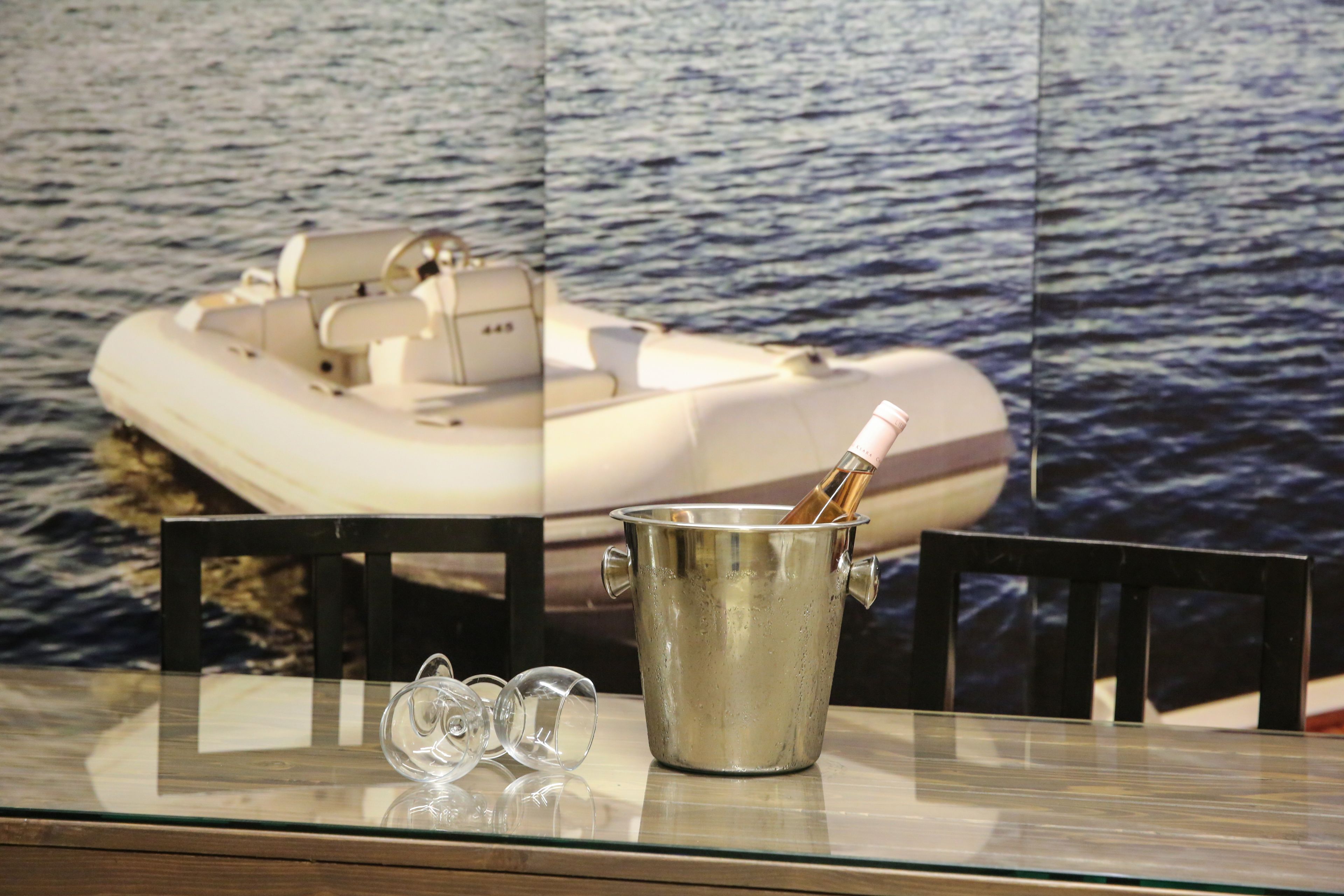 A glass table with a metal bucket containing a bottle, two empty glasses, and a chair.