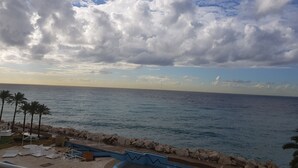 A coastal view with a rocky shoreline, palm trees, and a clear sky. - Four Seasons Halat (Halat)