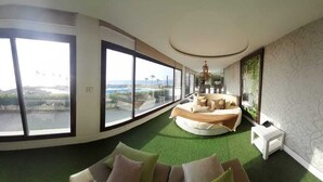 A modern living room with large windows, a circular seating area, and a view of a body of water. - Four Seasons Halat (Halat)