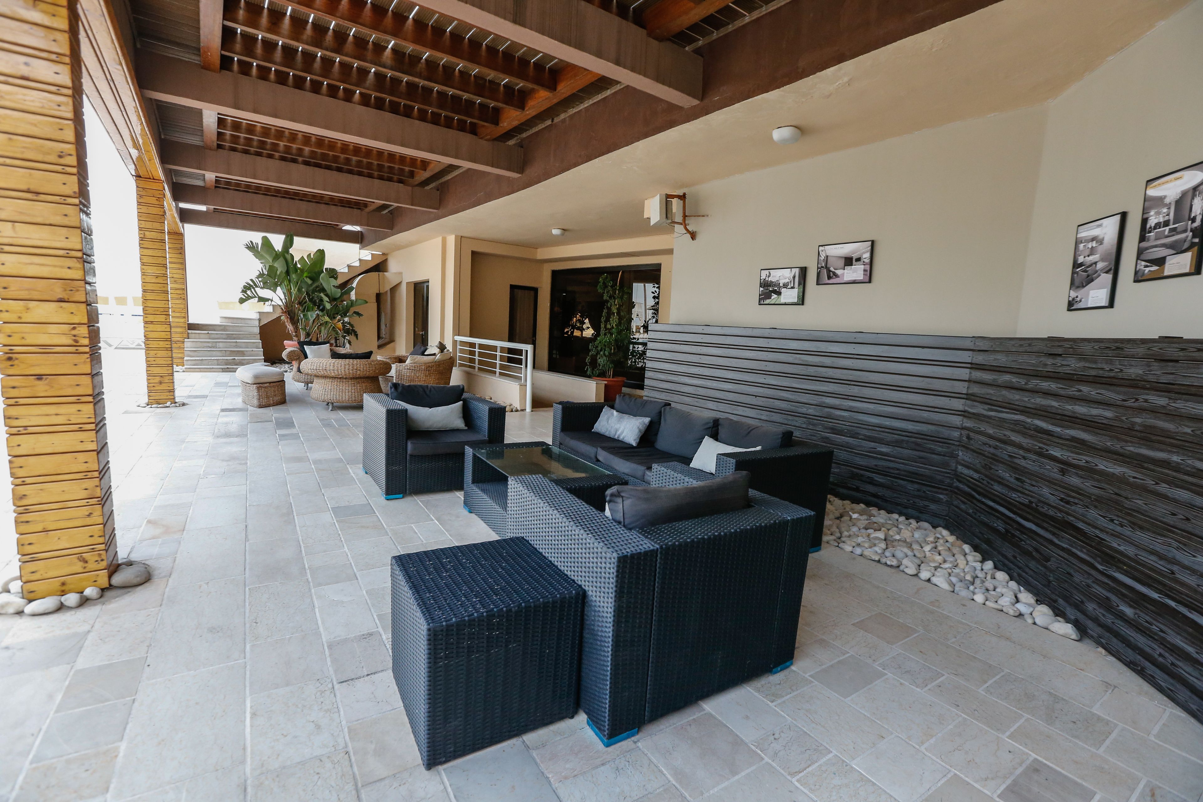 A spacious outdoor lounge area with wicker furniture, a stone floor, and a wooden ceiling.
