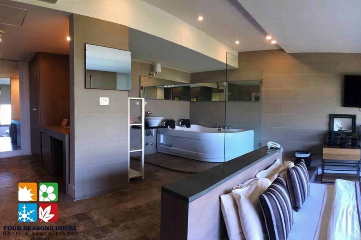 Une chambre d’hôtel moderne dotée d’un grand lit, d’une salle de bain séparée avec baignoire, d’un téléviseur fixé au mur et d’une grande fenêtre laissant entrer la lumière naturelle.