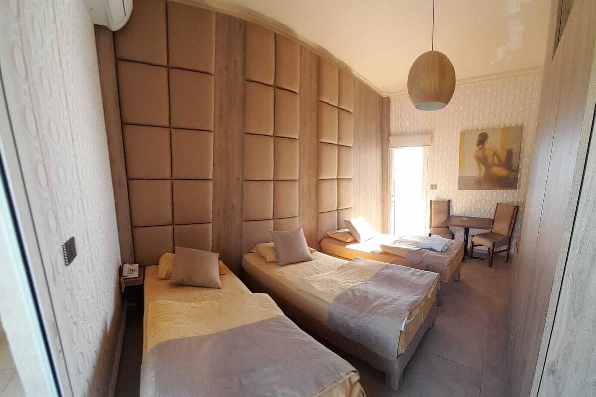 Une chambre d’hôtel avec deux lits, une grande tête de lit rembourrée, une petite table et une chaise.