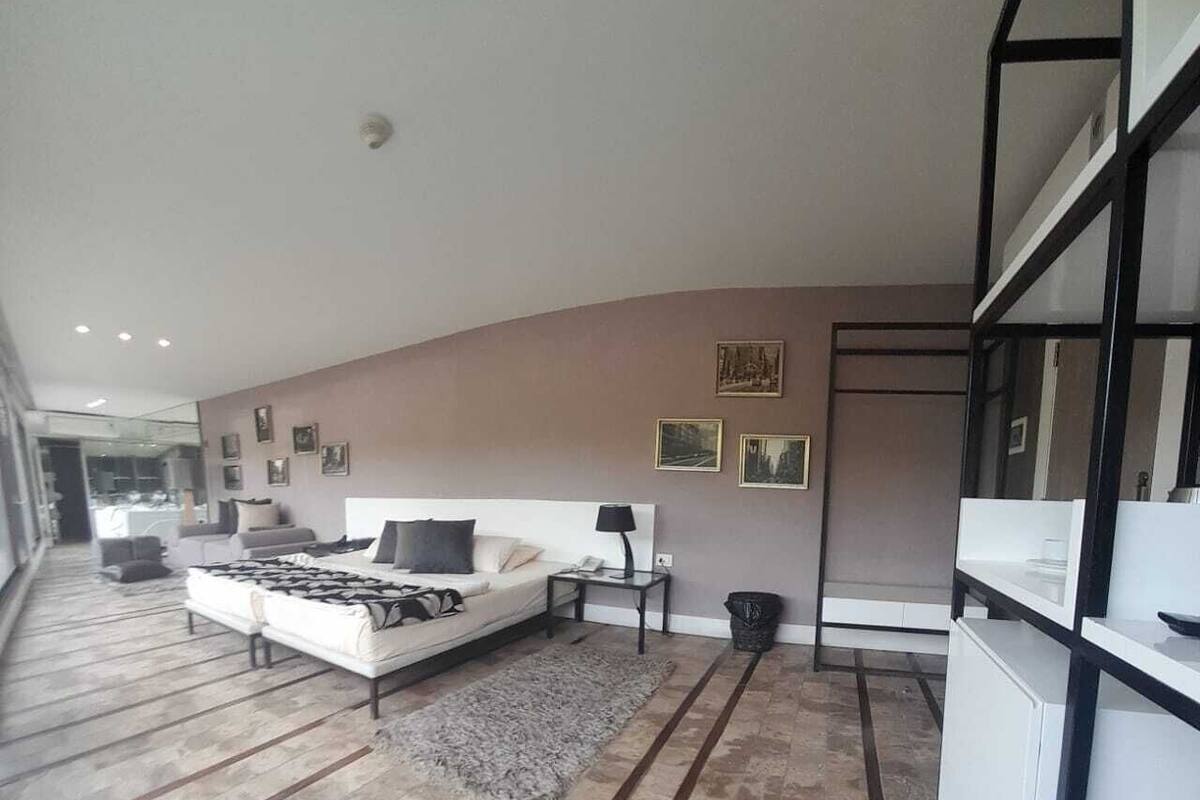 Une chambre à coucher moderne avec un grand lit, une table de chevet, une lampe et une petite poubelle.