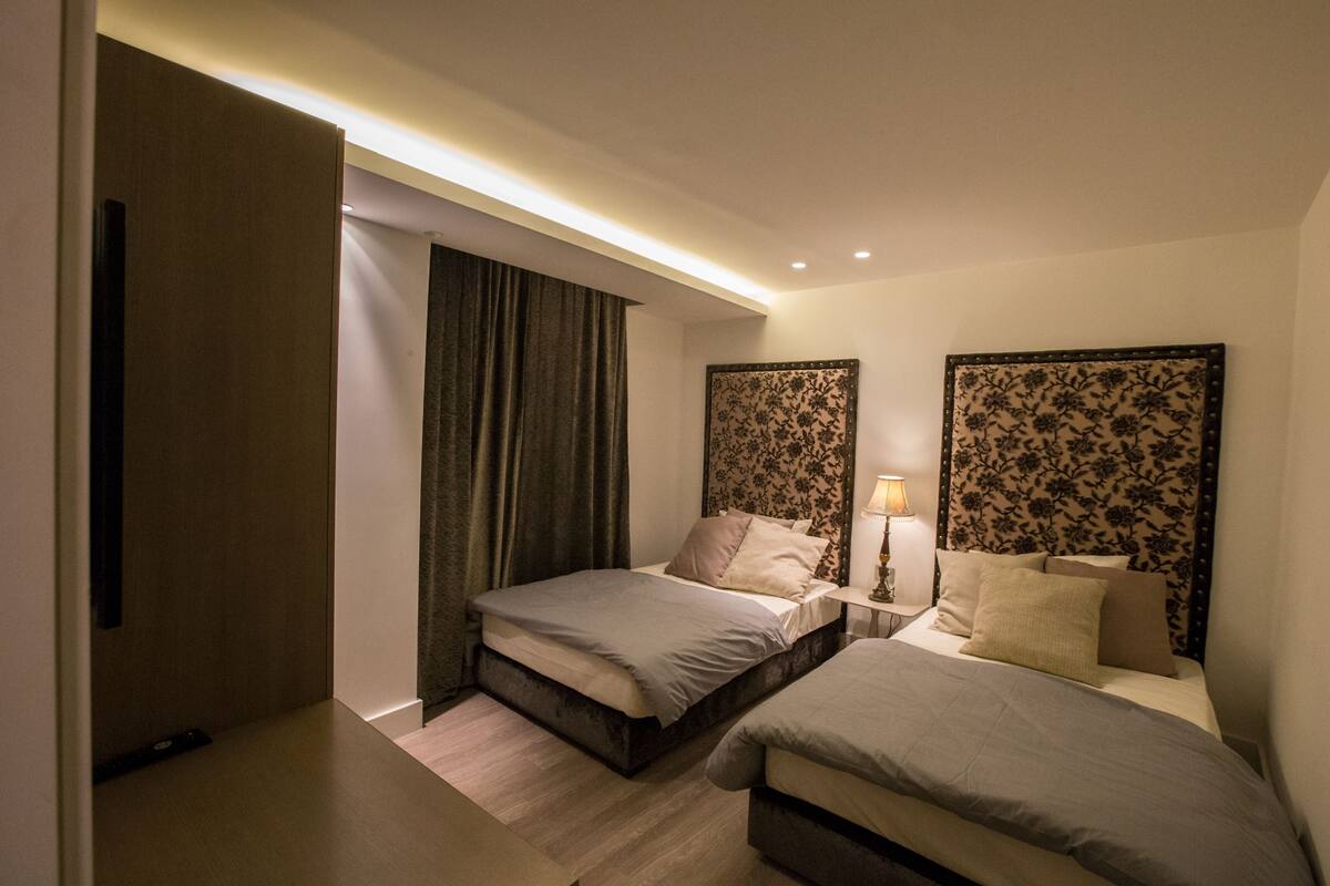 Une chambre d’hôtel comprenant un lit, une table de chevet, une lampe et une tête de lit ornée d’un motif floral.
