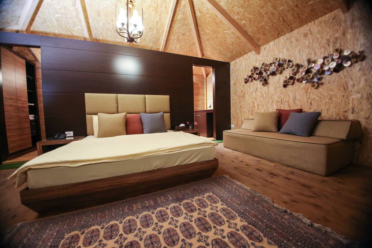 Une chambre avec un grand lit, un canapé, un plafond en bois et un mur décoré d’assiettes.