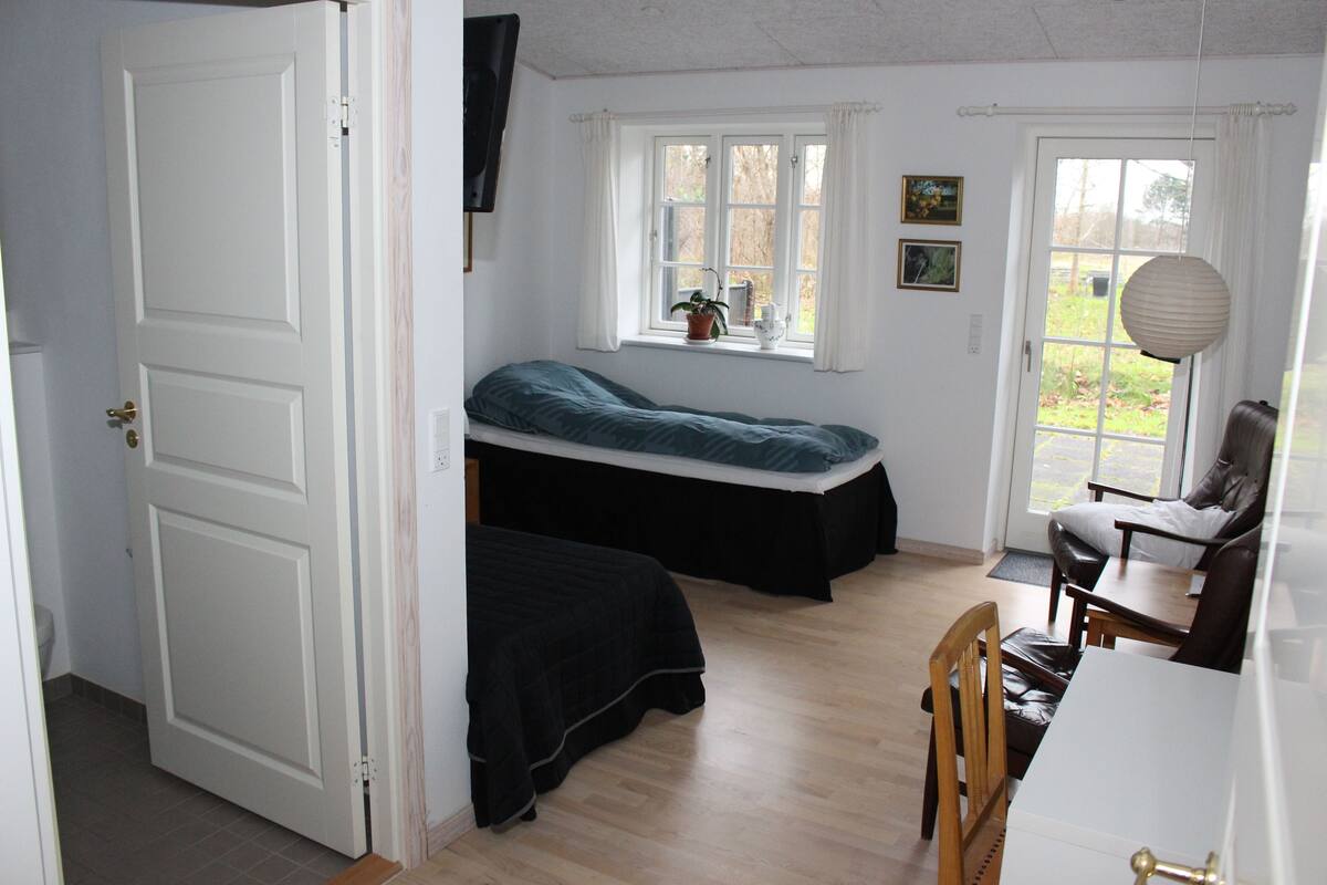 A bedroom with a bed, a desk, a chair, a window, and a door.