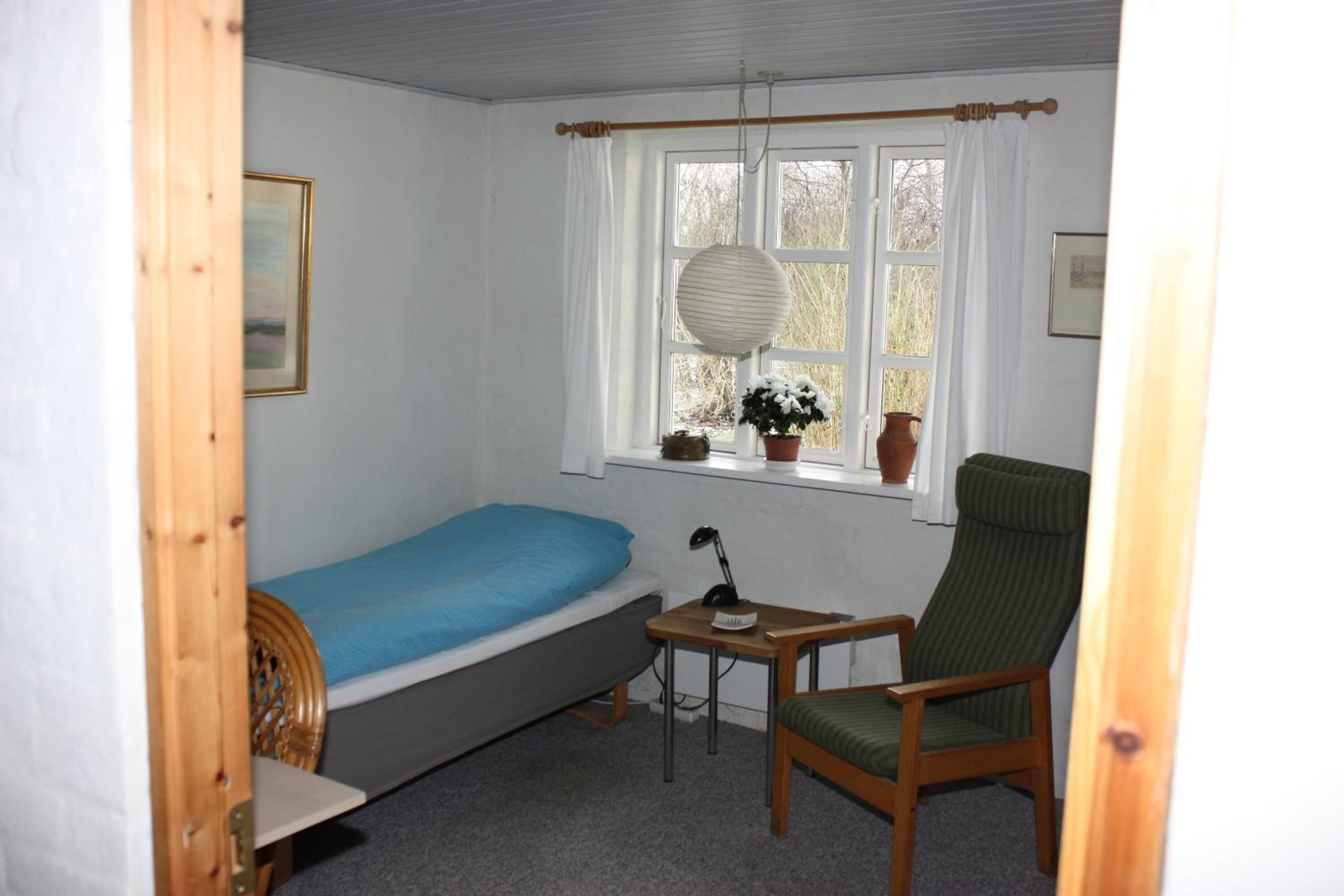 A small, single-room accommodation with a bed, a chair, a table, and a window with curtains.