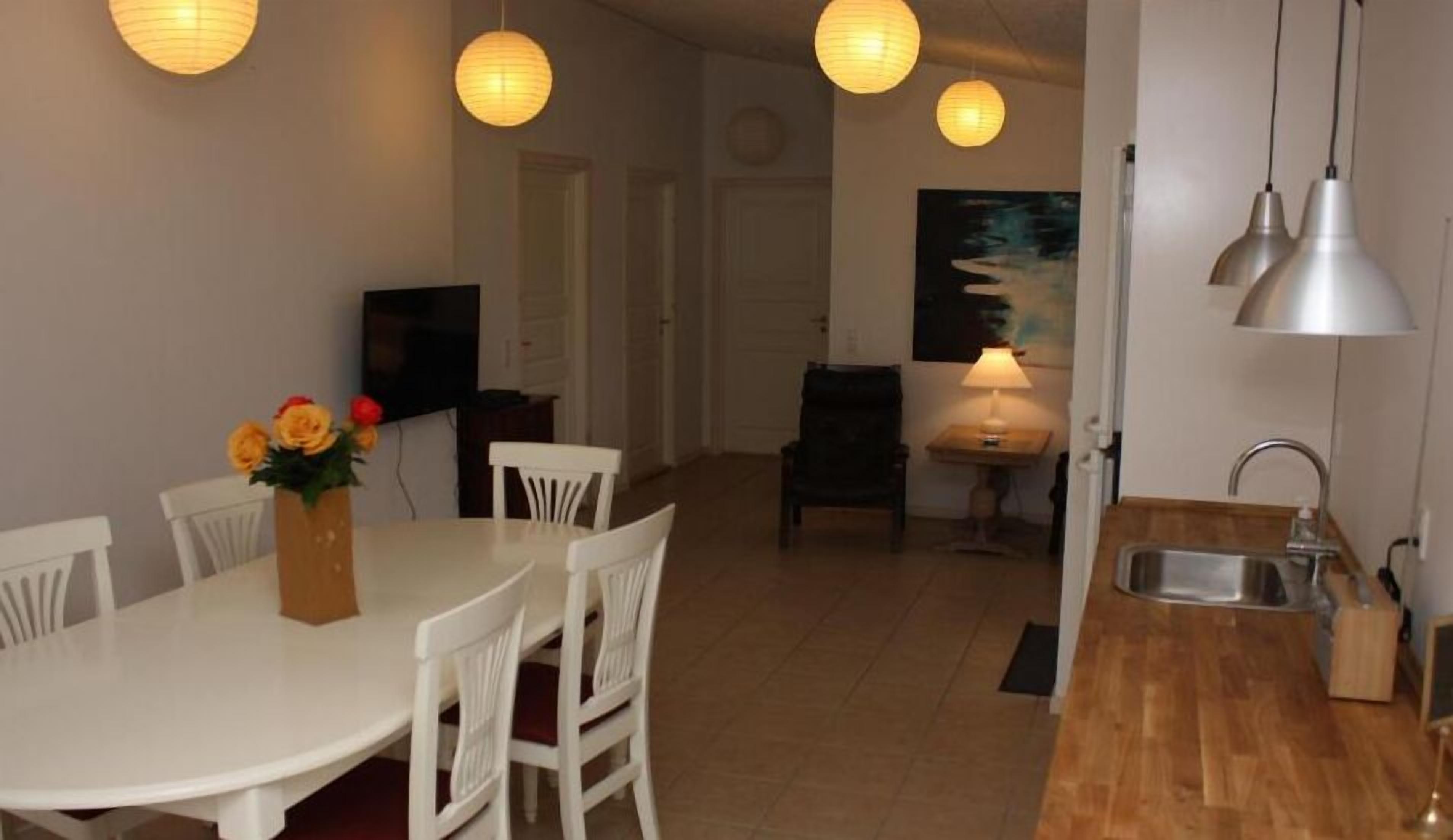 Un coin repas avec une table et des chaises blanches, un vase rempli de fleurs et un tableau accroché au mur.