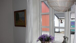 Een slaapkamer met een enkel bed, een klein tafeltje met een lamp, een raam met uitzicht en een hangende lamp.