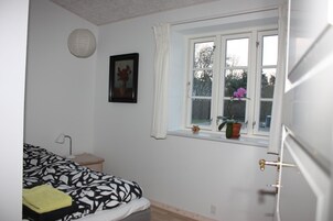 Un dormitorio con cama, mesita de noche, lámpara, ventana con cortinas e imagen enmarcada en la pared.