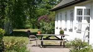 Een wit gebouw met een zwart dak, een picknicktafel en plantenbakken.