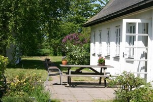 Un edificio blanco con techo negro, una mesa de picnic y plantas en macetas.