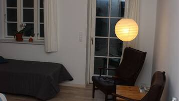 Una habitación con cama, escritorio, silla y mesa. Hay una ventana con cortinas, una planta en maceta y una lámpara colgante.