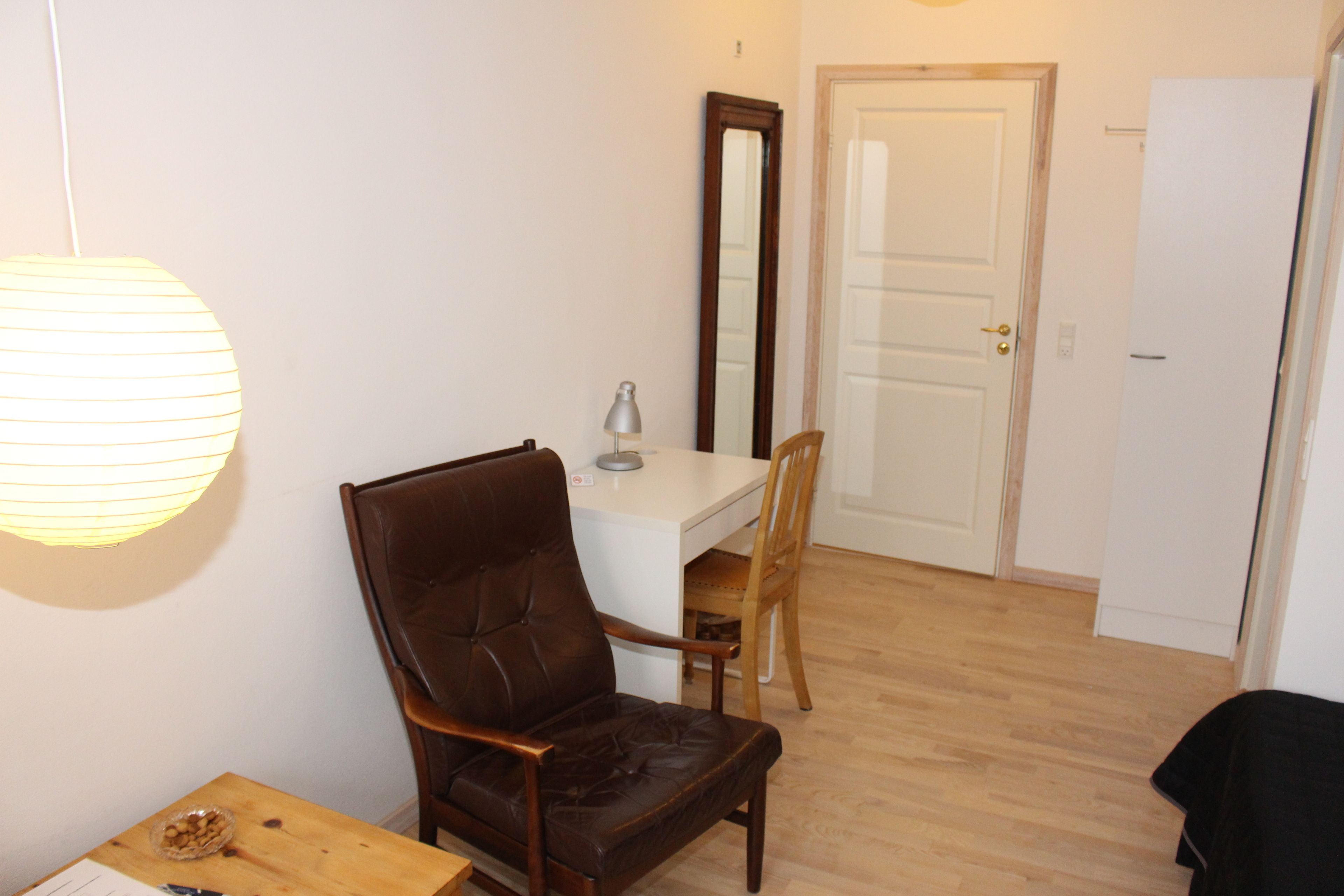 A room with a wooden dining table, two chairs, a lamp, and a mirror on the wall.