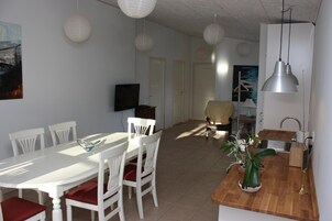 Un comedor con mesa y sillas blancas, una cocina con fregadero, y una sala de estar con sofá.