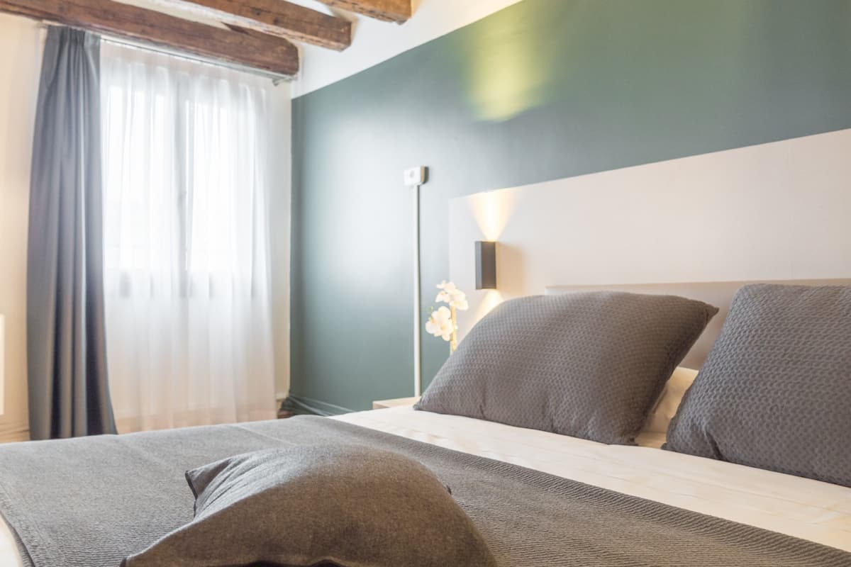 Ein Schlafzimmer mit Bett, Nachttisch, Lampe und einem Fenster mit Vorhängen.