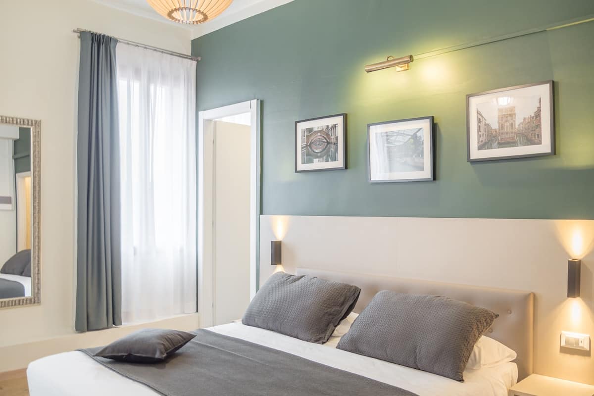 Ein ordentlich eingerichtetes Schlafzimmer mit einem Bett, zwei Nachttischen und einem großen Fenster mit Vorhängen.