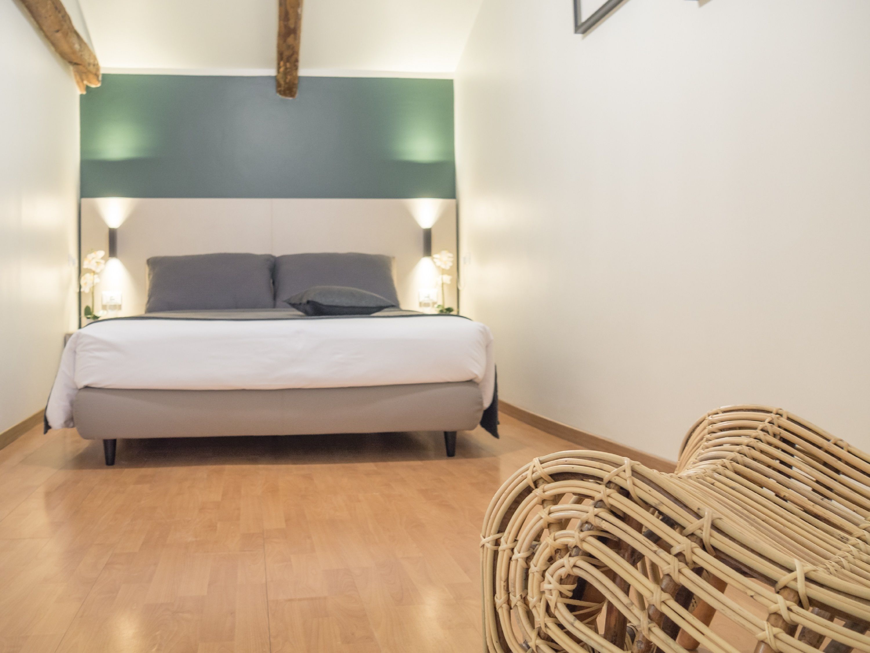 A neatly arranged bedroom with a bed, bedside lamps, and a wicker chair.