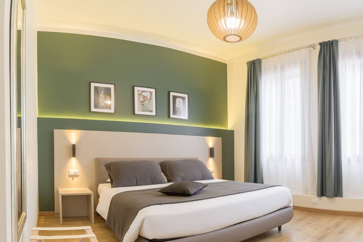 Ein modernes Schlafzimmer mit einer gebogenen Kopfteil, einem Bett mit grauer Bettwäsche, zwei Nachttischen und einer Pendelleuchte.