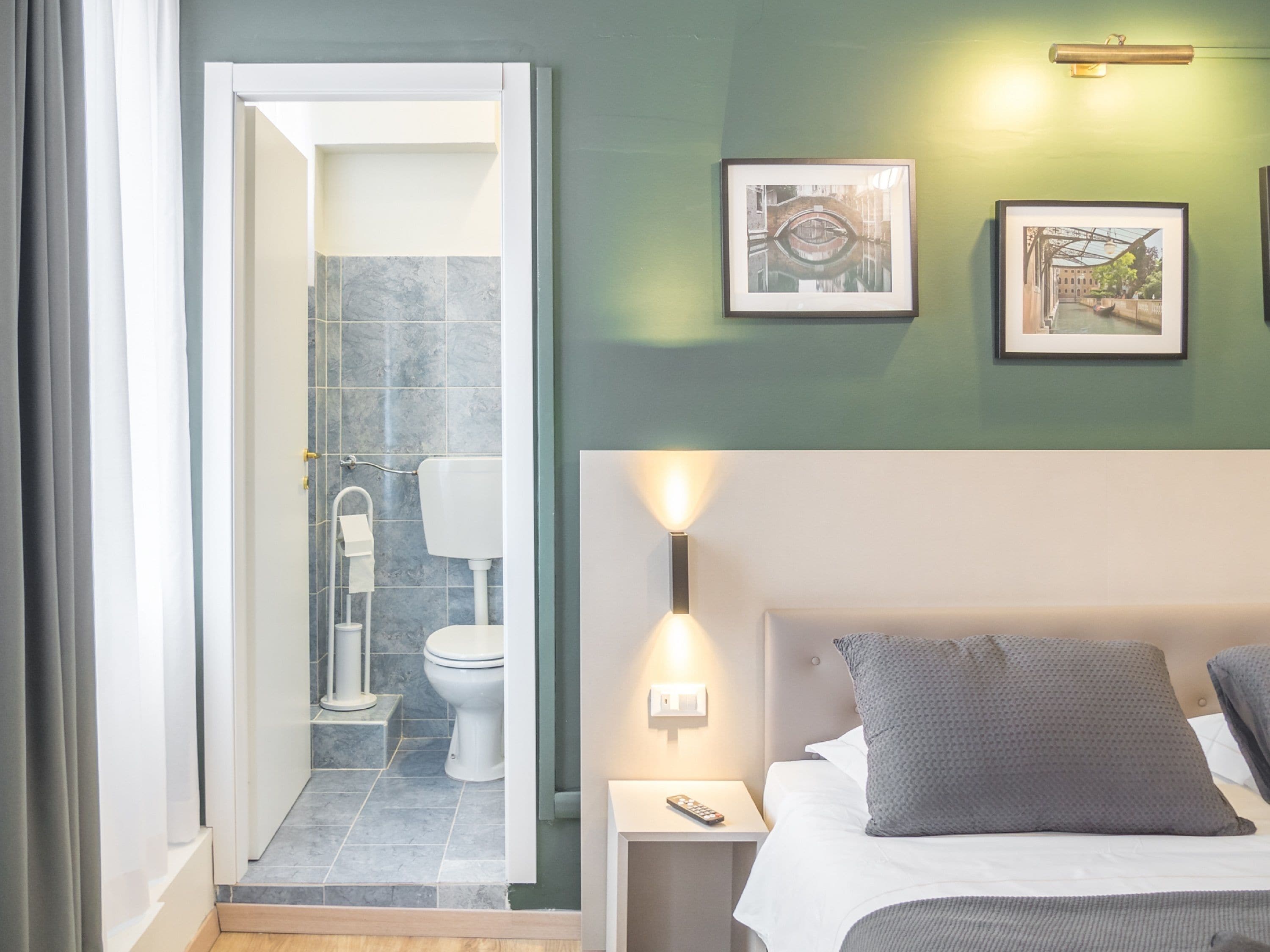 A hotel room with a shower, toilet, bed, bedside table, and wall-mounted artwork.
