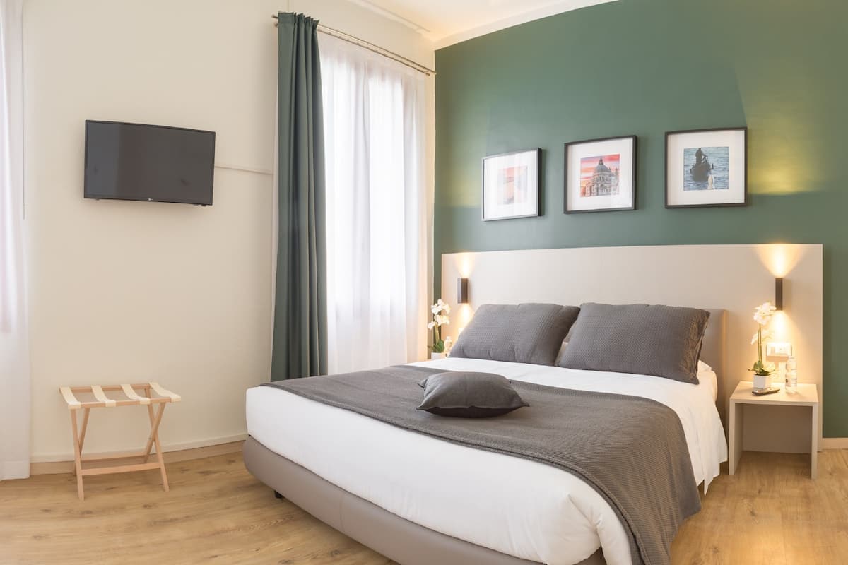 Ein ordentlich eingerichtetes Schlafzimmer mit Bett, Nachttischen, einem Fernseher und gerahmten Bildern an der Wand.
