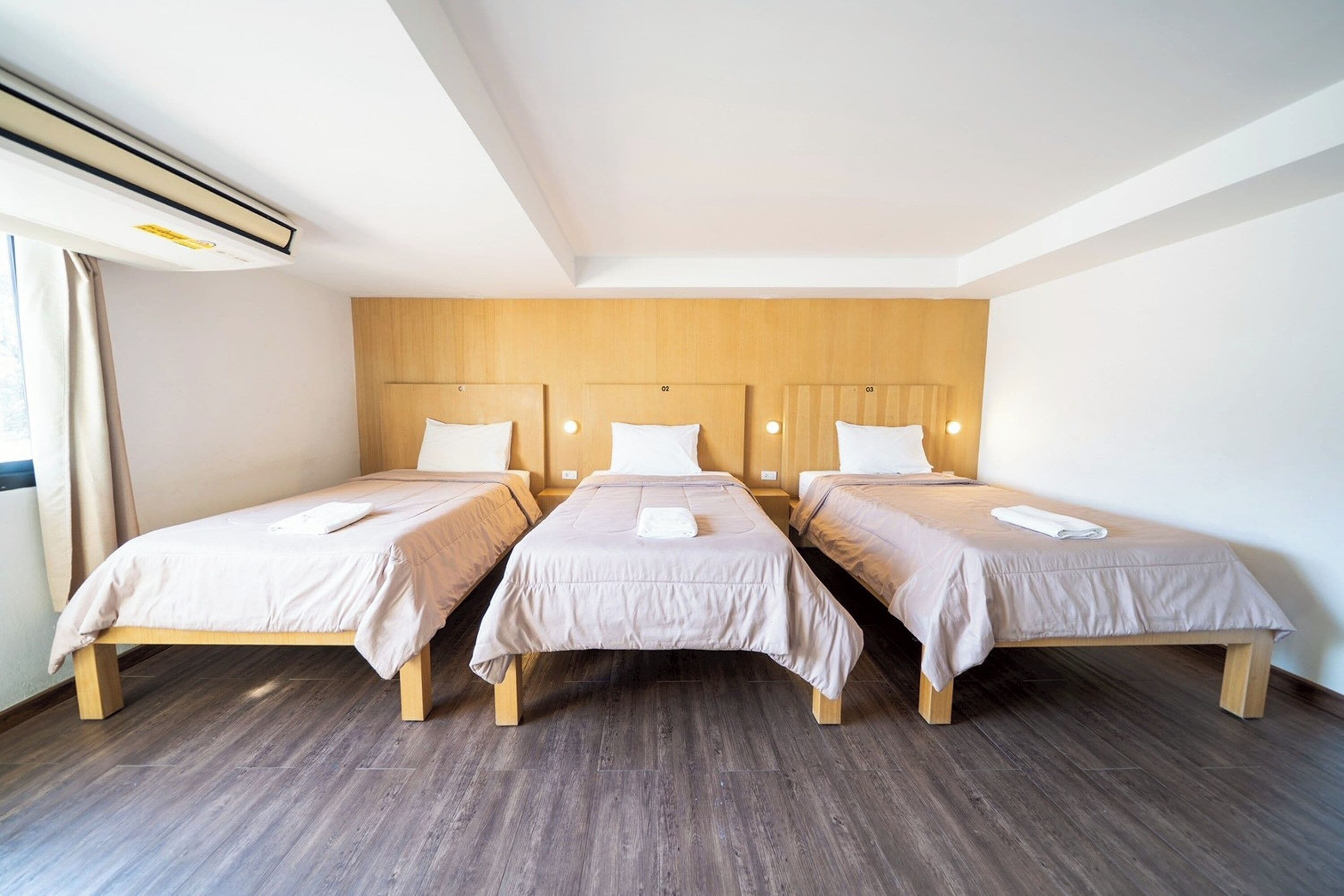 A hotel room with three single beds, wooden headboards, and a large window with curtains.