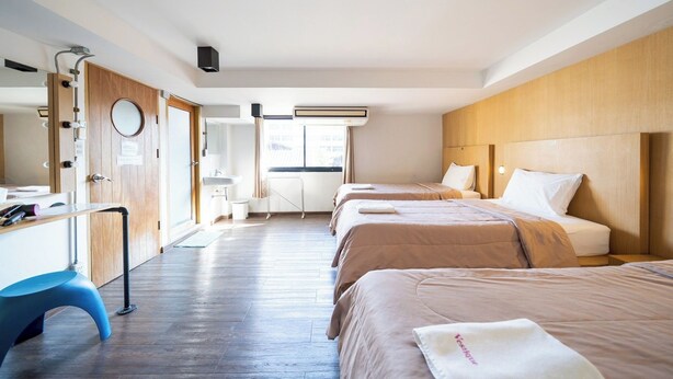 Habitación de hotel con tres camas, un escritorio, un espejo y una ventana con cortinas.
