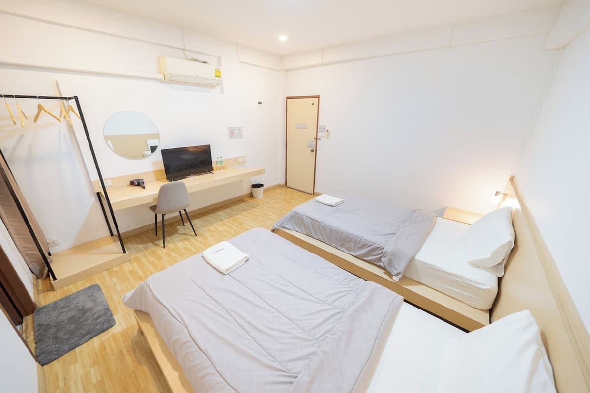 A hotel room with two beds, a desk with a computer, a chair, a mirror, and a wardrobe.