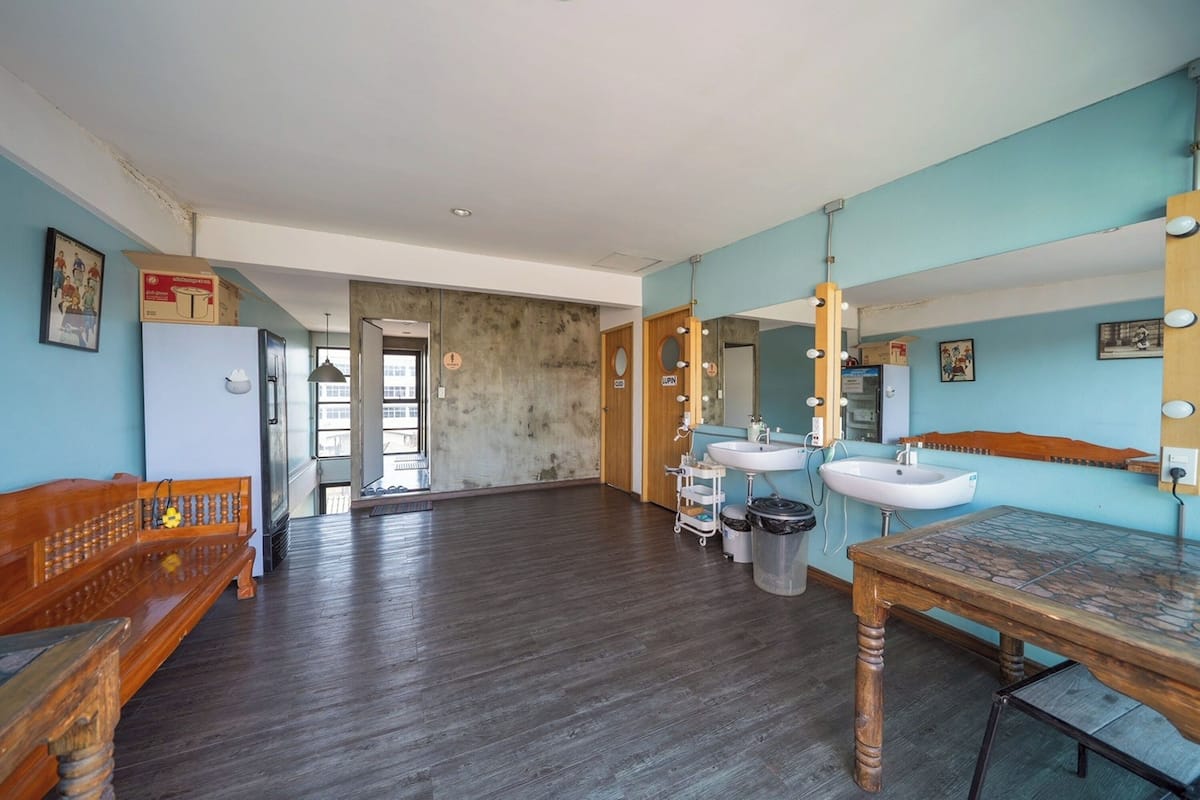 A room with a wooden bench, a table, a sink, and a mirror with lights.