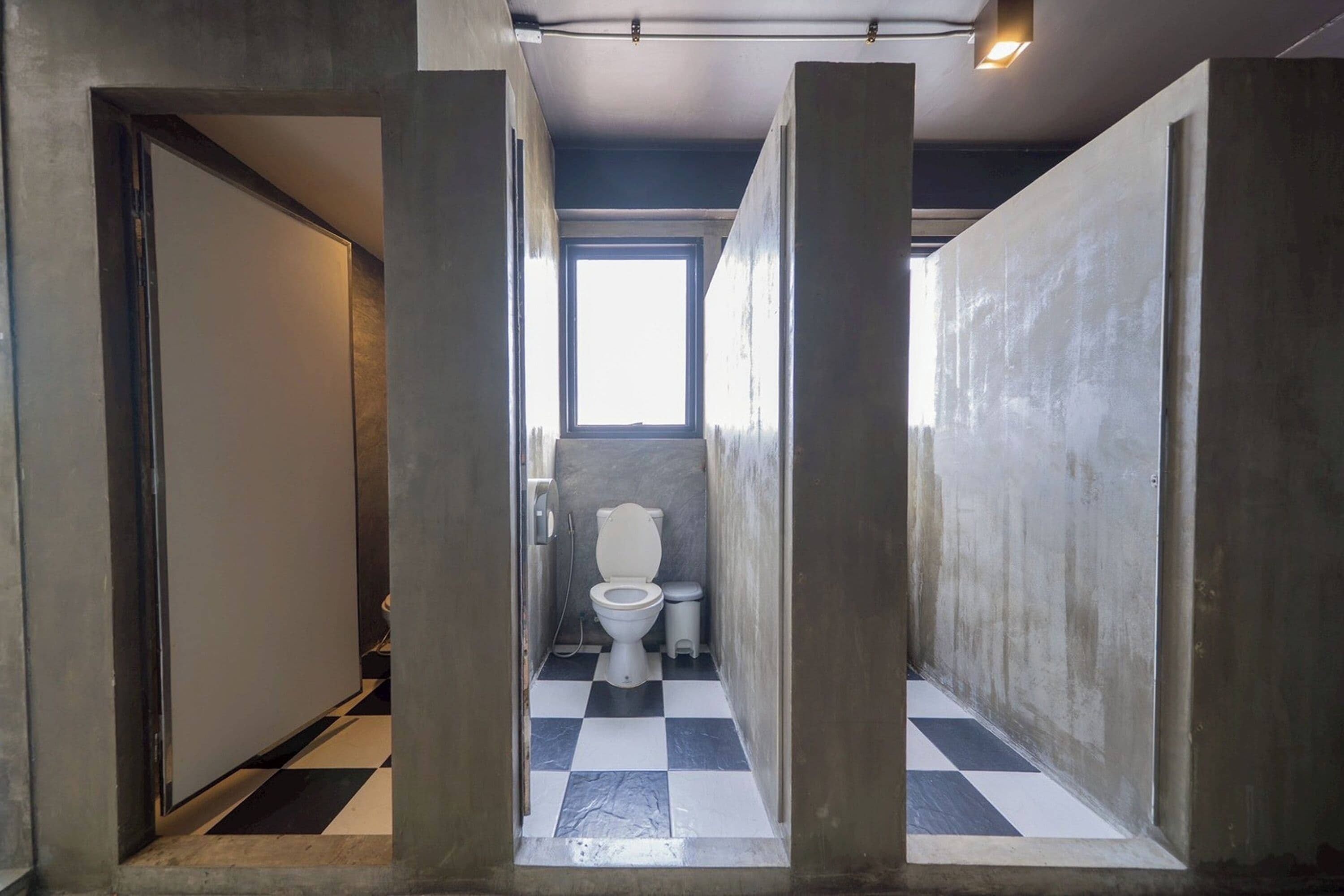 Ein schmaler Gang mit Schachbrettmuster, der zu einem Sanitärbereich mit Fenster über der Toilette führt.