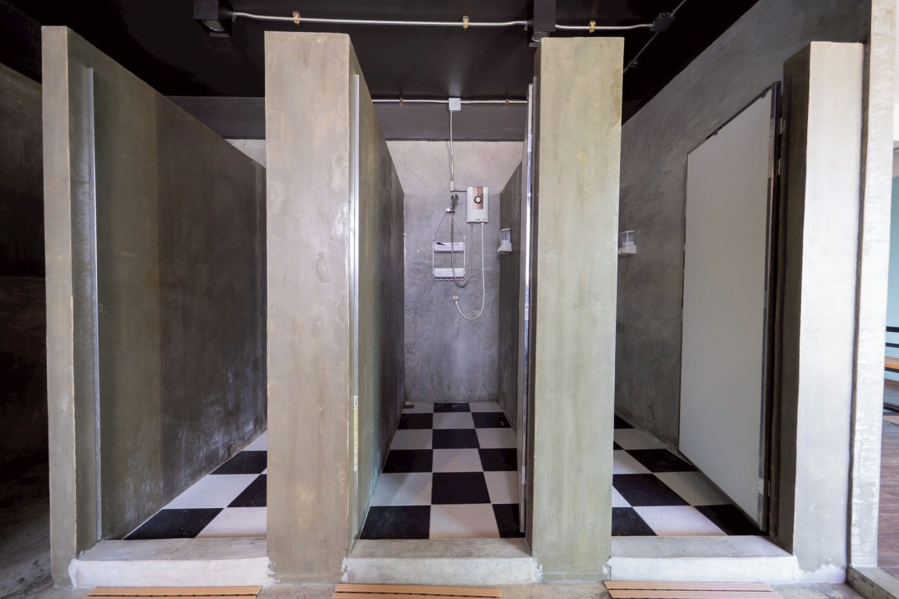 A narrow hallway with checkered flooring, concrete pillars, and a shower area with a control panel.